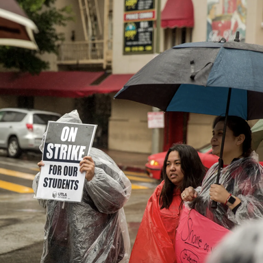 Several women stand under umberellas with signs that say 'On Strike for our Students'