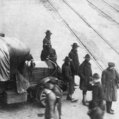 A black-and-white photo of the Seattle strike: several men in coats standing in front of a canvas-covered truck