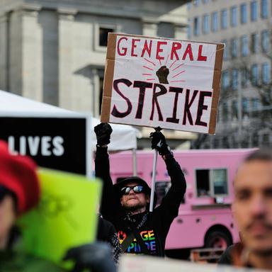A man holding a sign in the midst of a protest that says 'General Strike'